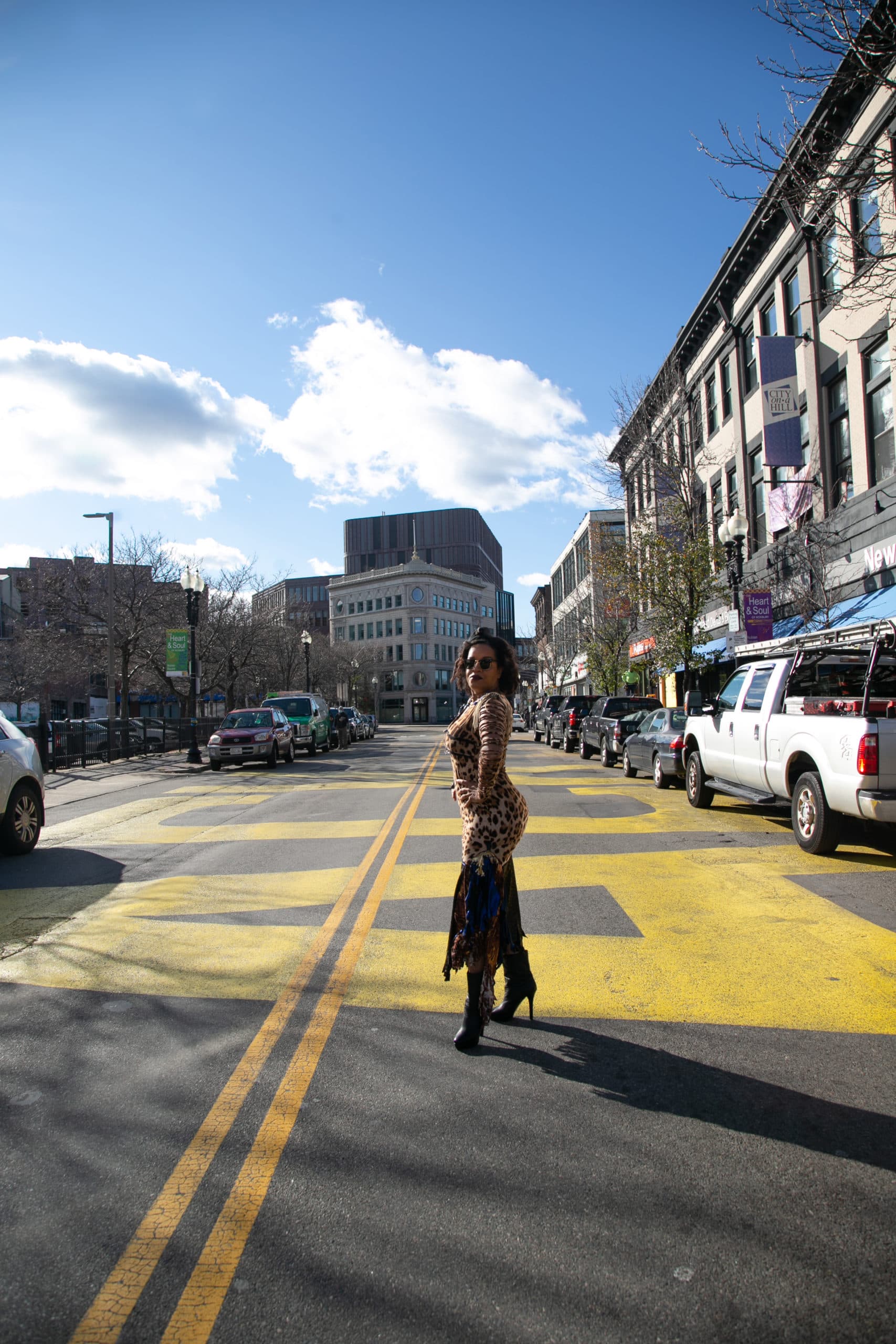 Kai Grant stands by the Black Lives Matter mural, featuring bright yellow lettering, beneath a blue sky.