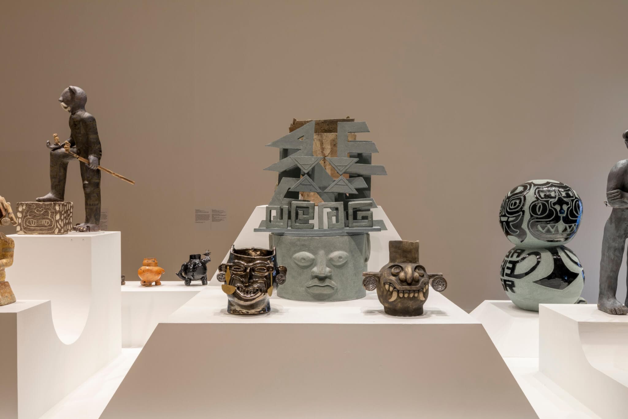 Statues, figurines, and more adorn white platforms at Tufts University Art Galleries.